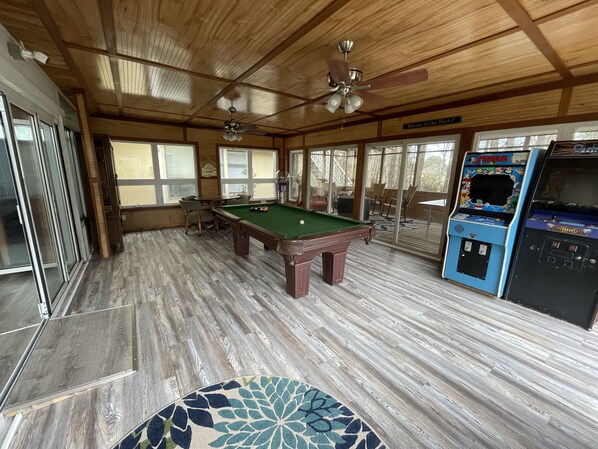 A wooden interior with a pool table, arcade games, and a ceiling fan.