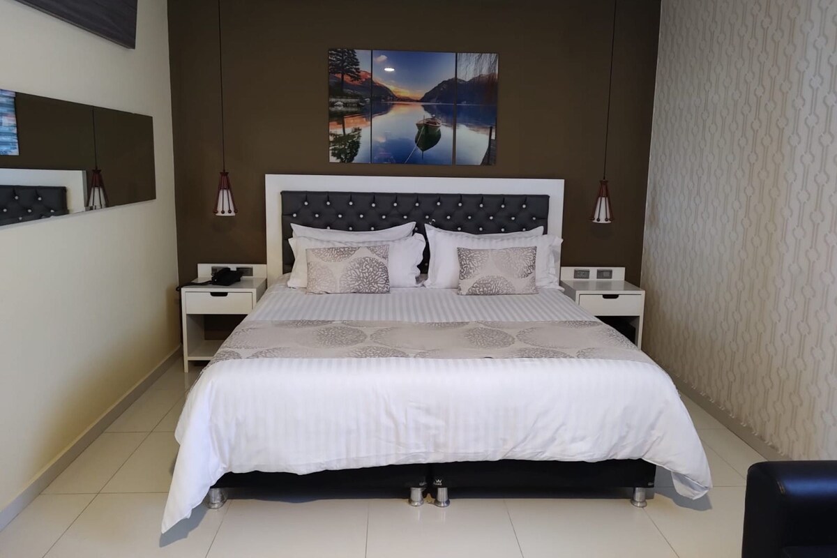 Ein Schlafzimmer mit einem großen Bett, zwei Nachttischen, einem Wand-Fernseher und einem Bild über dem Bett.