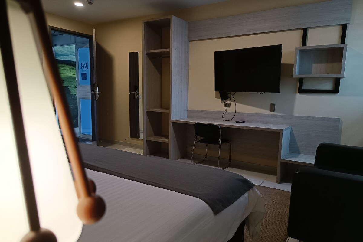 Ein Hotelzimmer mit Bett, Schreibtisch, Stuhl, Fernseher und Kleiderschrank.