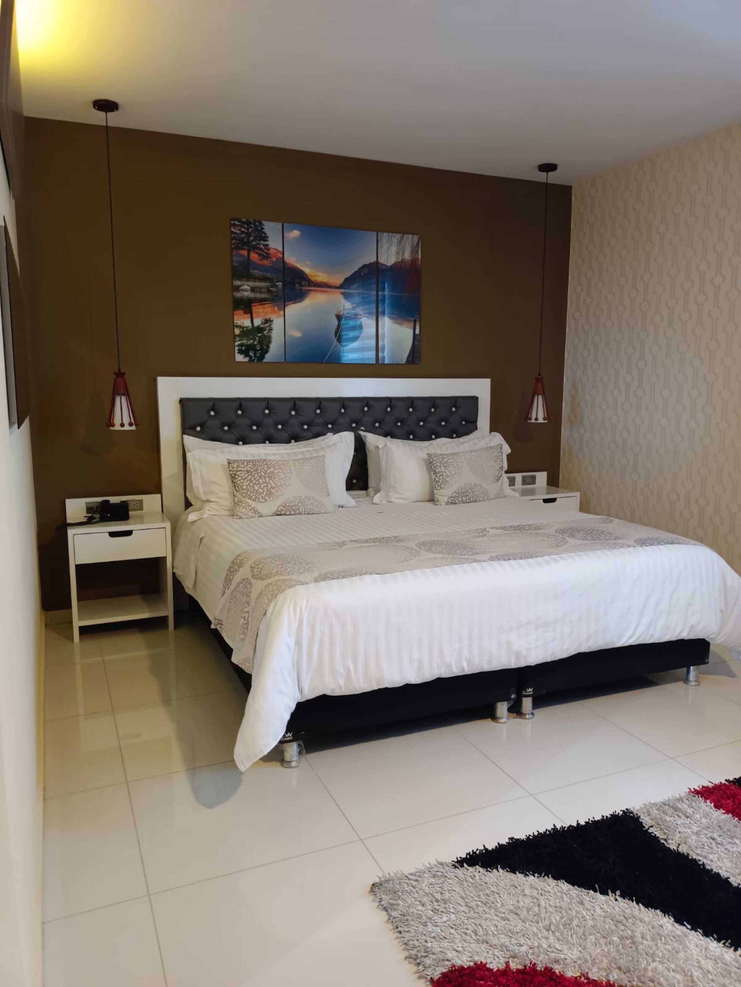 Een slaapkamer met een groot bed, een nachtkastje, een aan de muur hangend schilderij en een kamerkleed met een patroon.