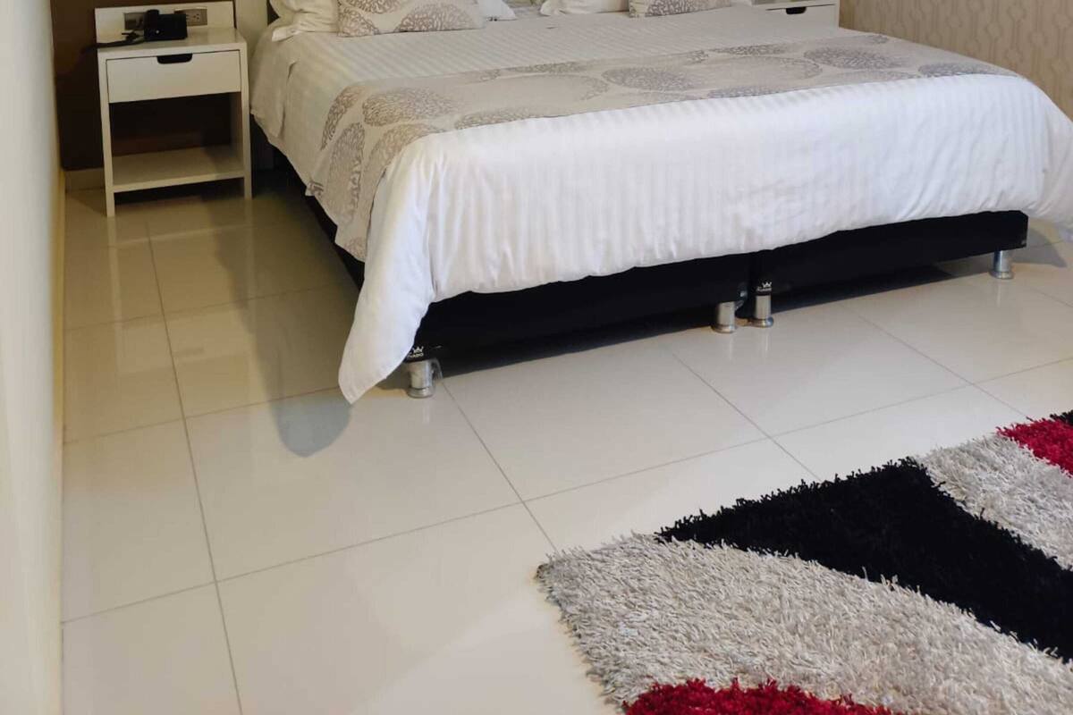 A bedroom with a large bed, a nightstand, a wall-mounted painting, and a patterned rug.