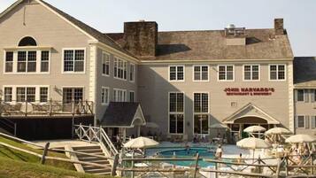 Un edificio de dos pisos con piscina, asientos al aire libre y un letrero que dice 'John Harvard's Restaurant & Brewery'.