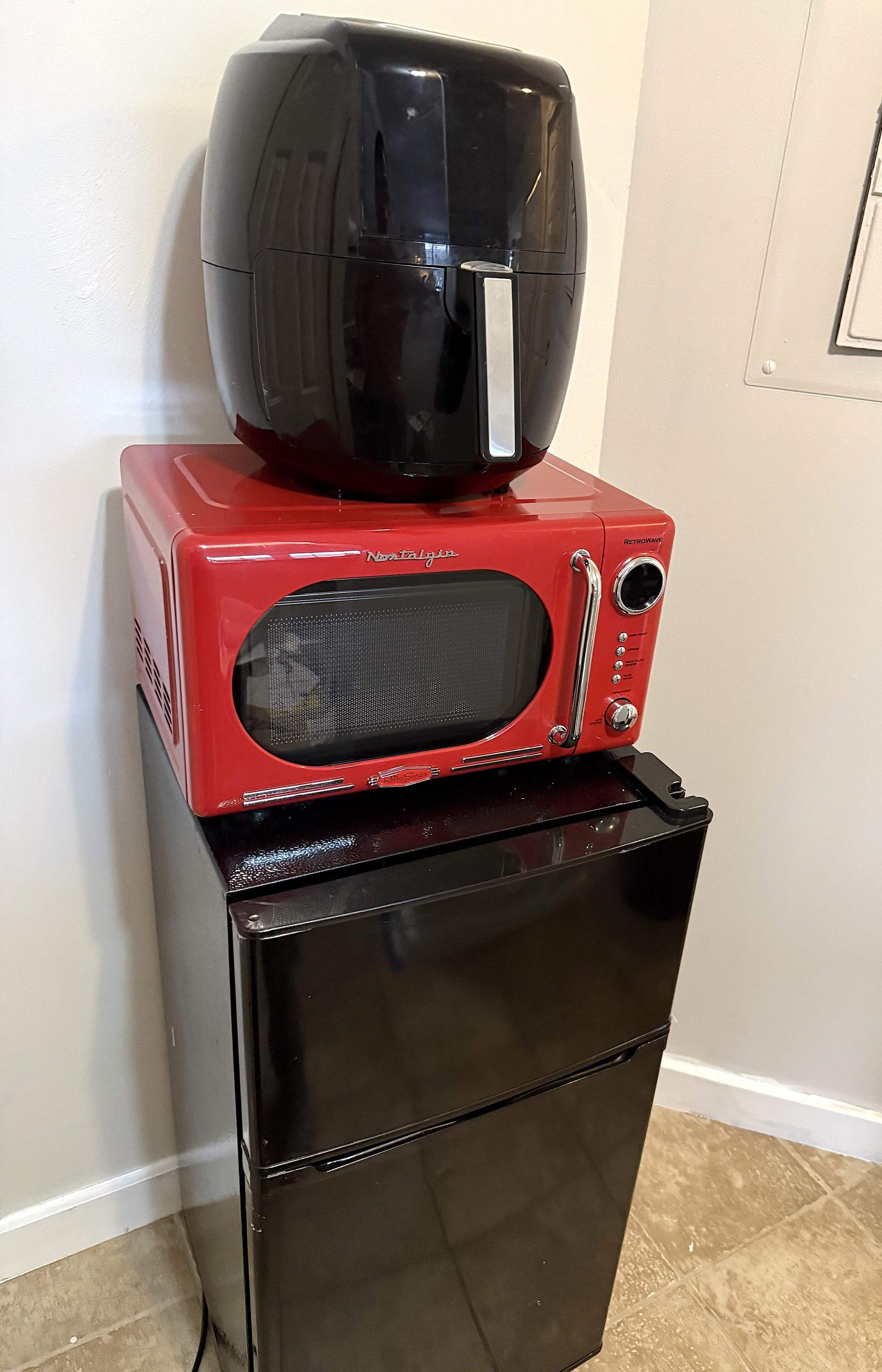 Uma geladeira preta com um micro-ondas vermelho em cima.