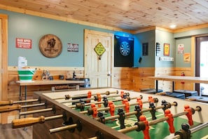 Una habitación con mesa de futbolín, dardos y una zona de bar.