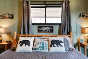 A bed with two pillows, a wooden headboard, a window with curtains, a sign above the window, and a lamp on each side of the bed. - Cozy Mountain Cabin, dark skies, and great views! (West Branch Township)
