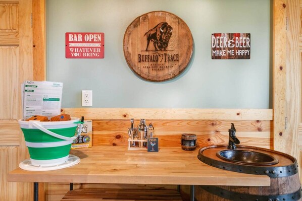A bar area with a wooden sign, a bucket of snacks, a bottle of whiskey, and a beer tap. - Cozy Mountain Cabin, dark skies, and great views! (West Branch Township)