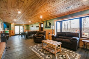 L’intérieur chaleureux du chalet est doté d’un plafond en bois, d’un coin repas, d’une cheminée et d’une grande fenêtre offrant une vue sur l’extérieur.