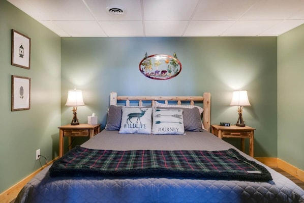 Un dormitorio con una cama, dos mesitas de noche, dos lámparas, un reloj de pared y una lámpara de techo.