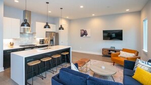 A modern kitchen with a central island, bar stools, pendant lighting, and a dining area with a sofa and coffee table. - Close to it all*Rooftop*Photo Walls*BBQ on Roof (Nashville,)