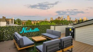 A rooftop patio with seating and a neon sign reading "Nashville". - Close to it all*Rooftop*Photo Walls*BBQ on Roof (Nashville,)