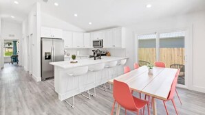 Una cocina moderna con armarios blancos, un refrigerador de acero inoxidable y una isla central con taburetes de bar.