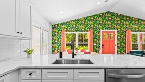 Una cocina moderna con armarios blancos, un lavamanos de acero inoxidable y una puerta roja.