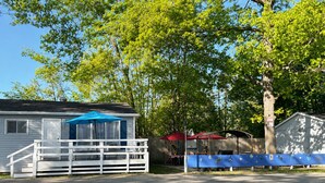 Ein kleines Haus mit Veranda, einem blauen Sonnenschirm und einem eingezäunten Bereich mit Grill.
