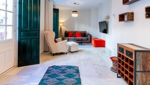 A modern living room with a sofa, armchair, and a coffee table. There is a TV mounted on the wall and a wooden cabinet with drawers. - Holi-Rent Peñuelas (Sevilla)