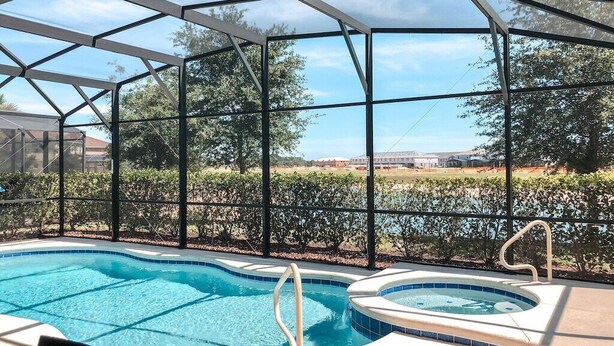 Una piscina con cerramiento de vidrio, rodeada de una estructura metálica y vista a un lago y árboles.