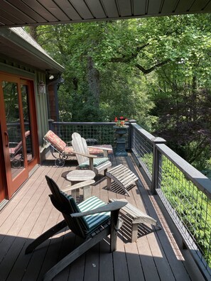 Une terrasse en bois, aménagée avec du mobilier d’extérieur, notamment des chaises et une table, qui offre une vue sur une forêt verdoyante et luxuriante.