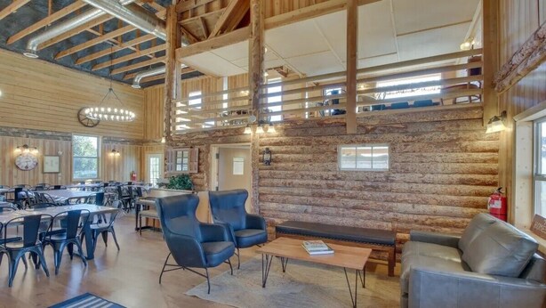 A spacious indoor area with a high ceiling, wooden beams, and a stone wall. There are multiple tables and chairs arranged for dining or meetings. - Bear Lake Sleeps 44 Private Inn  Family Reunions Groups (Paris)
