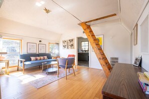 Un salón amplio con suelo de madera, un sofá azul, una escalera de madera y una cocina al fondo.