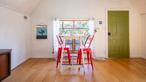 A room with a wooden floor, a green door, a window with curtains, and a table with red chairs. - The Bohemian - A Hill Country Cottage (San Marcos)