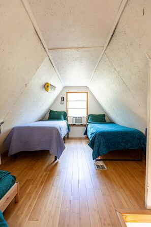 Une petite chambre mansardée avec deux lits, une fenêtre et un ventilateur de plafond.