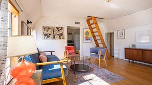 A living room with a sofa, chairs, a coffee table, a lamp, a ladder, and artwork on the walls. - The Bohemian - A Hill Country Cottage (San Marcos)
