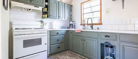 Una cocina con estufa, horno, lavabo y una licuadora integrada.