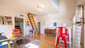 A spacious living area with a wooden floor, a glass coffee table, and a red chair. - The Bohemian - A Hill Country Cottage (San Marcos)