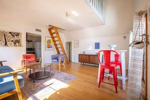 A spacious living area with a wooden floor, a glass coffee table, and a red chair.