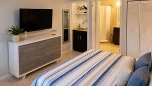 Une chambre à coucher comprenant un lit, un téléviseur, un ventilateur de plafond, une commode, une salle de bain avec douche et un placard.
