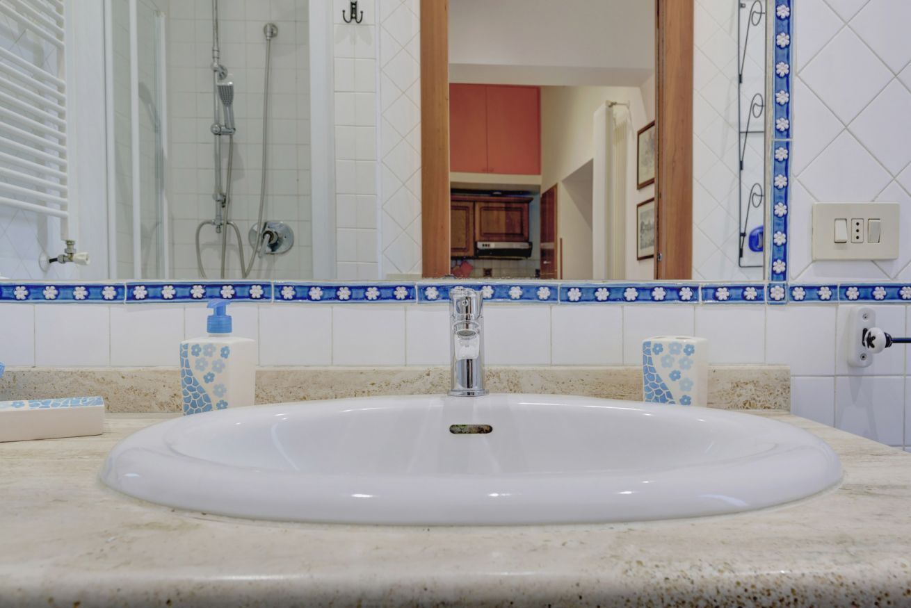 Une salle de bain avec un lavabo blanc, des carreaux bleus et blancs à motifs, une douche en verre et une vue sur une partie de la cuisine.