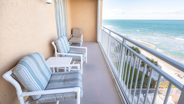 A balcony with white wicker furniture, a white table, and a view of the ocean. - Oceanfront 2BR Condo 6th Floor Corner Unit Indian Harbour Beach, 601 (Indian Harbour Beach)