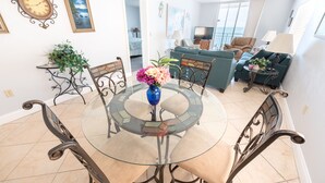 A dining area with a glass table surrounded by chairs, a sofa, and a TV in the background. - Oceanfront 2BR Condo 6th Floor Corner Unit Indian Harbour Beach, 601 (Indian Harbour Beach)