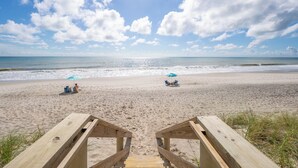 A beach with wooden boardwalks leading to the water, two umbrellas, and a clear sky. - Oceanfront 2BR Condo 6th Floor Corner Unit Indian Harbour Beach, 601 (Indian Harbour Beach)