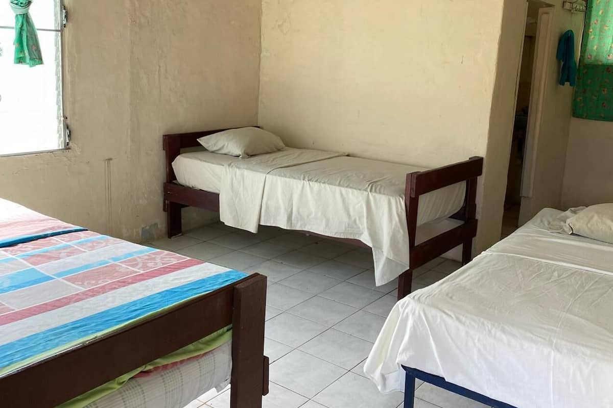 Quarto de dormitório com duas camas individuais, uma mesa de madeira e uma janela com cortina.