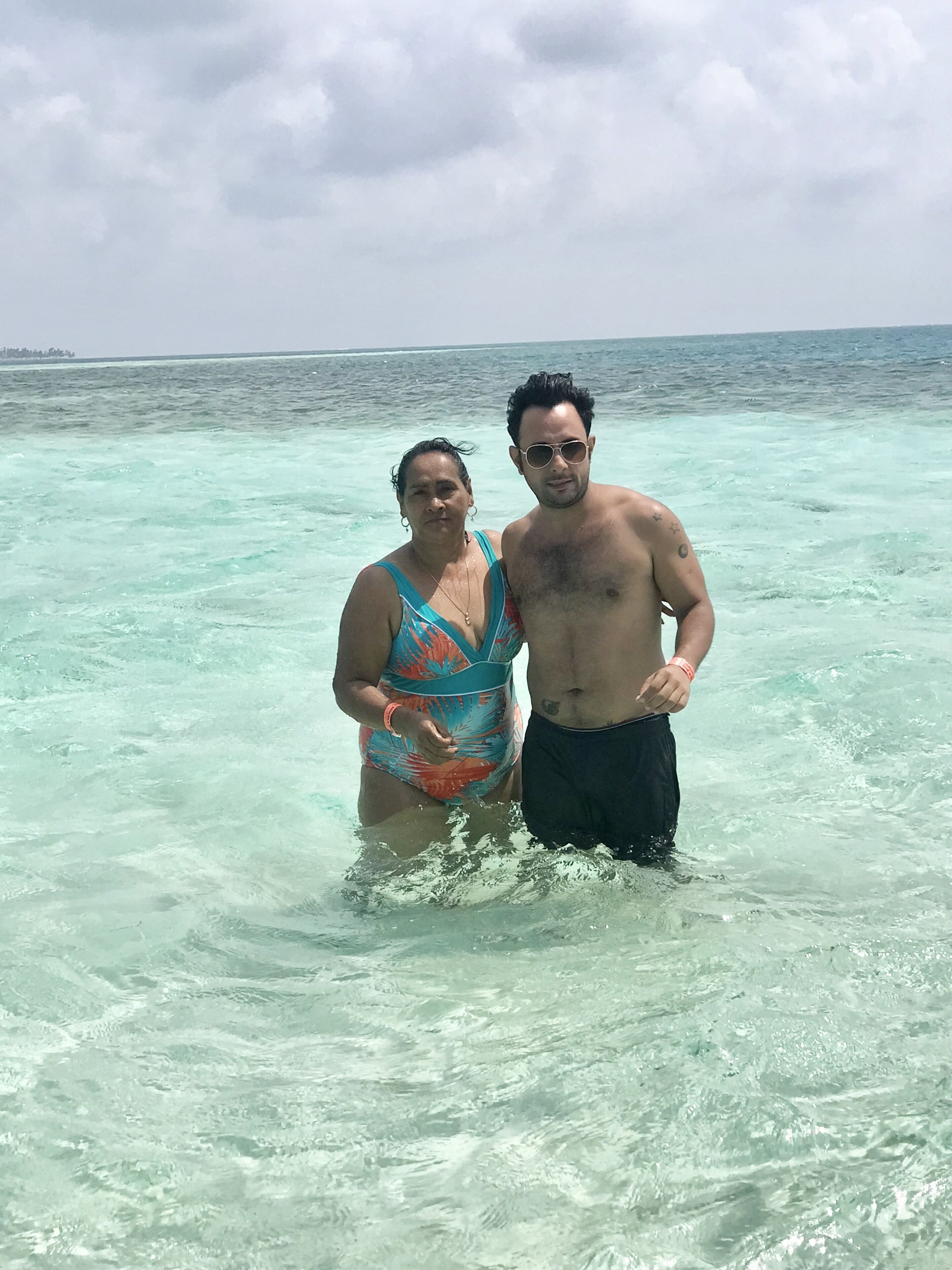 Dos personas de pie en agua poco profunda y transparente, con una orilla lejana.