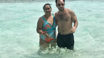 Dos personas de pie en agua poco profunda y transparente, con una orilla lejana.