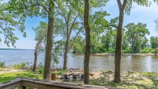 A lakeside camping area with a wooden deck, chairs, and trees. - Mighty Mississippi River Retreat (Scott County)