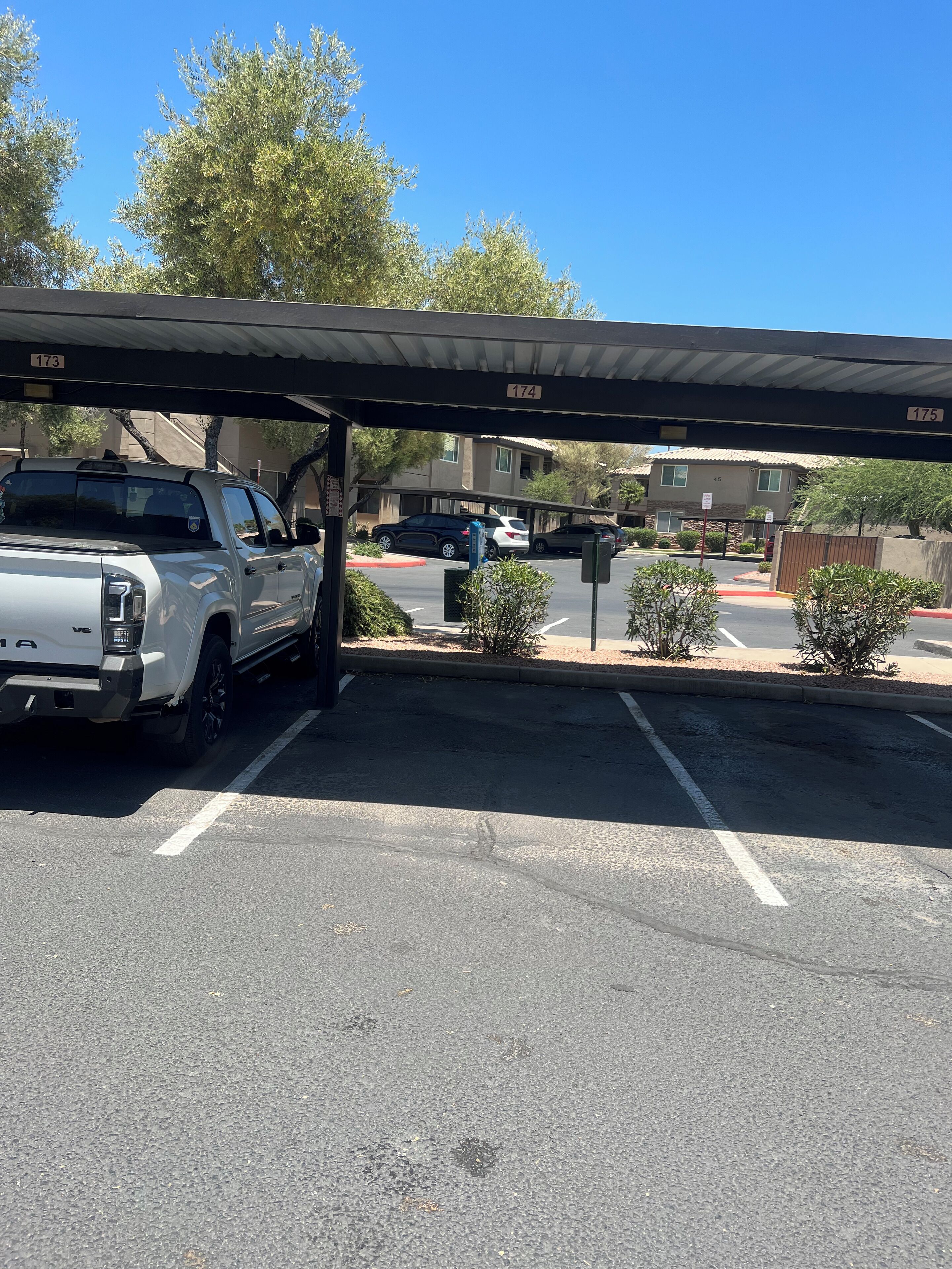A parking area with a covered section, a white truck, and a building in the background.