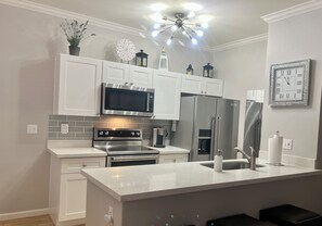 A modern kitchen with white cabinetry, a central island, stainless steel appliances, and decorative items on the shelves.