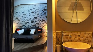 Ein Schlafzimmer mit einem Bett, einer Steinwand und einem Badezimmer mit einem runden Spiegel und Waschbecken.