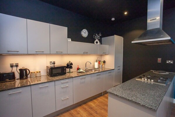 Una cocina moderna con armarios grises, microondas, hervidor y cocina a gas.