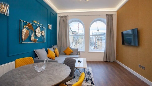 A modern living room with a city view, a round dining table, and a flat-screen TV mounted on the wall.
