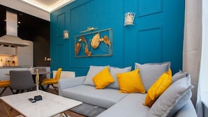 A modern living room with a blue accent wall, a grey sectional sofa with yellow cushions, a white coffee table, and a framed artwork.