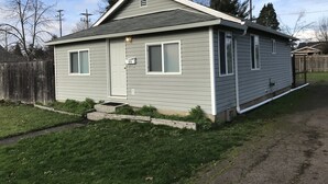 Une maison de plain-pied à l’extérieur gris, avec une porte d’entrée et deux fenêtres sur le côté.