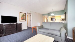 A living room with a flat-screen TV, dark wooden furniture, a grey sofa, and a small table. - Two Bedroom, Ocean Front, Luxury Condo, Indian Harbour Beach, FL 3208987 (Indian Harbour Beach)
