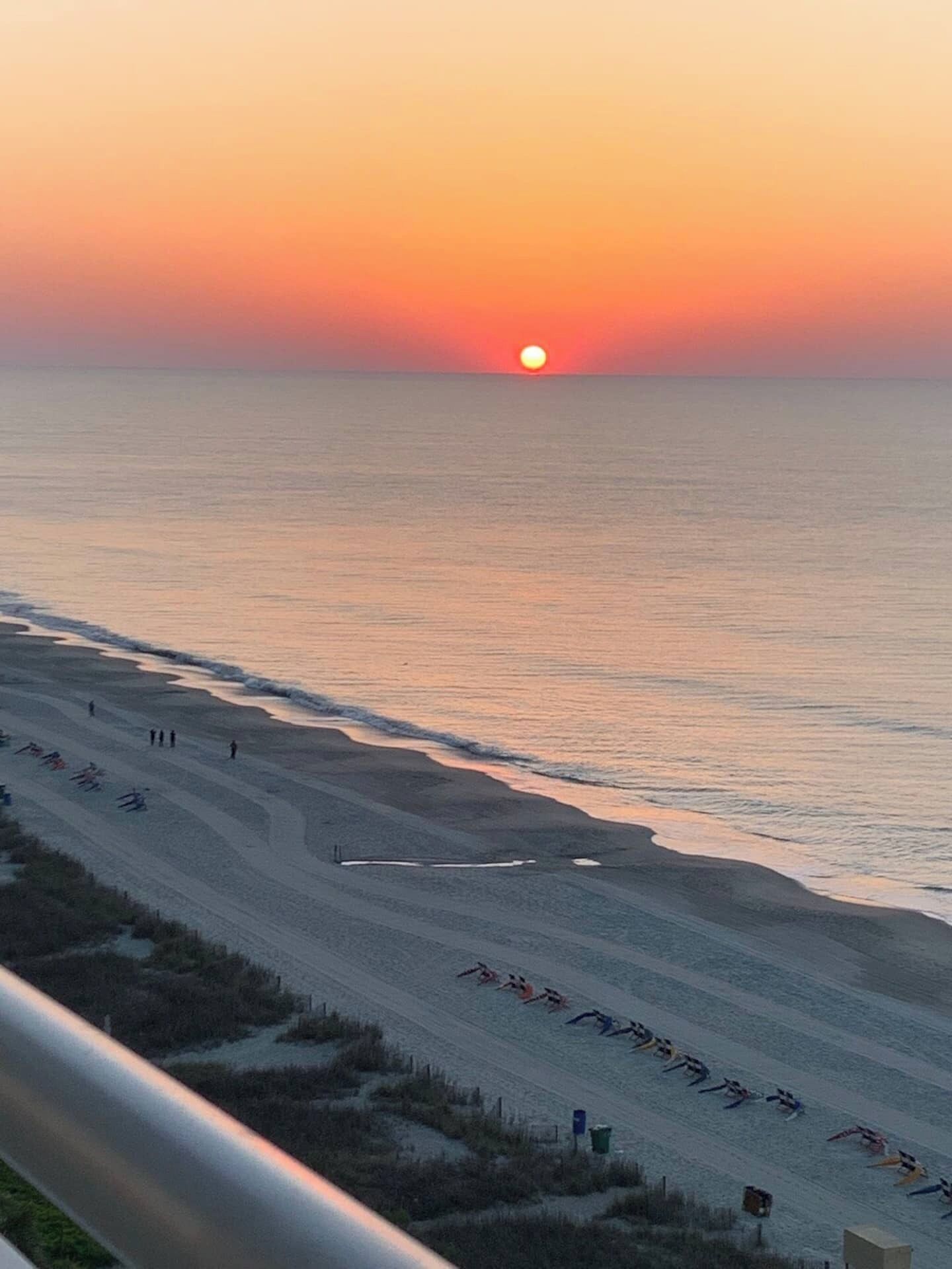 A beach at sunset with a row of beach chairs and umbrellas.