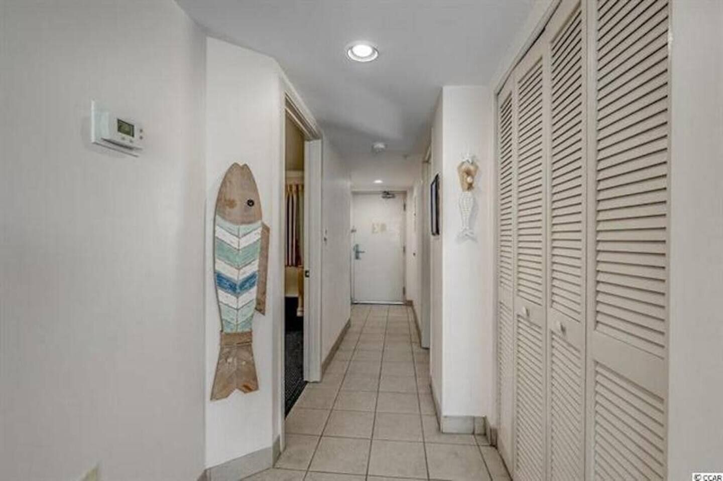 A narrow hallway with a tiled floor, a fish decoration on the left wall, and a door at the end.