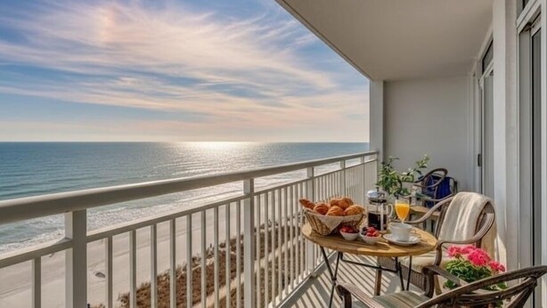 Un balcón con una mesa dispuesta para el desayuno, con vista a una playa y el océano.