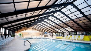 An indoor swimming pool with a high ceiling and glass panels, surrounded by white chairs and a yellow wall.