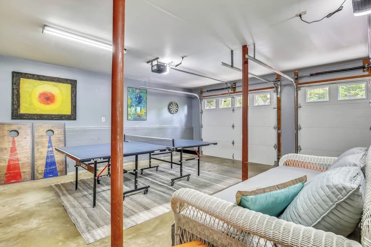 Una habitación con mesas de ping pong, un sofá de mimbre y un dardo.
